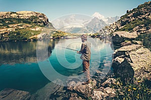 Young Man fishing on Lake with rod mountains landscape on background