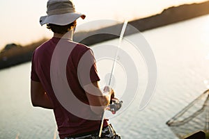 Young man fishing on lake at sunset enjoying hobby