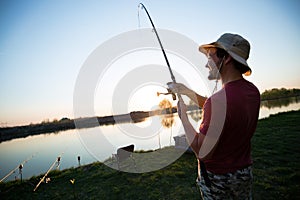 Young man fishing on a lake at sunset and enjoying hobby