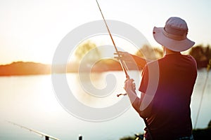 Young man fishing on a lake at sunset and enjoying hobby