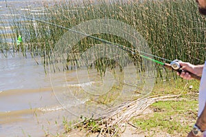 Young man fishing in pond, lake, closeup of fishing rod and reel