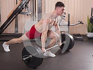 Young man flexing muscles with barbell in gym