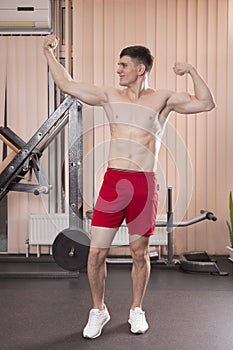 Young man flexing muscles with barbell in gym
