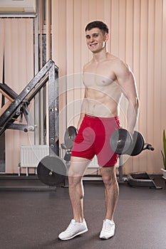 Young man flexing muscles with barbell in gym