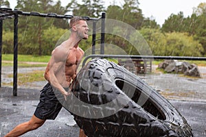 Young man flipping a tire. Heavy workout in a rainy day.