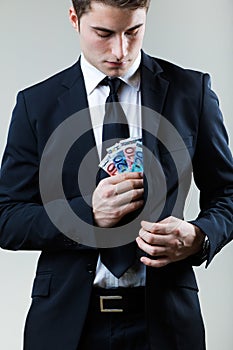 Young man in formalwear putting money in his pocket.