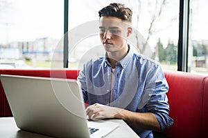 Young man freelancer chatting on mobile phone while sitting front open laptop computer in cafe