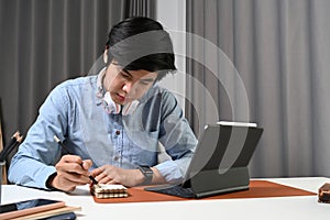 Young man freelancer with headphone sitting in home office and working with computer tablet.