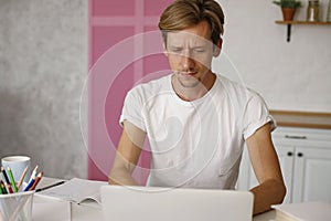 Young man freelancer using laptop studying online working from home, happy casual millennial guy typing on pc notebook surfing