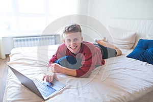 Young man freelancer works on a laptop at home in bed. Work on the Internet