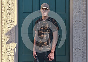 Young man in front of a green door with a camouflage t-shirt