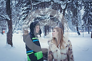 Young man in a fur hat with a earflap with a kitten in the hood of his jacket and a girl in a beige fur coat against the