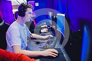 Young man gamer play online video games with headphones in internet club cafe, blue color. Esports concept photo