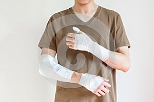 Young man with gauze bandage wrapped around his injured arms, knee at home. Man with hands wrapped in medical bandage on white