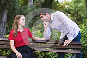 Young man gazing into the woman\'s eyes as she sits on a bench in the park
