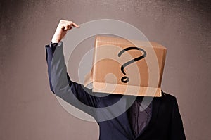 Young man gesturing with a cardboard box on his head with question mark photo