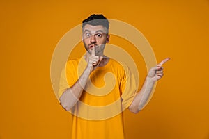 Young man gesturing silence sign and pointing finger at copy space isolated