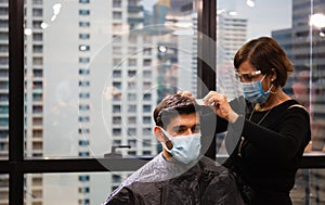Young man getting haircut by hairdresser, Barber using scissors and comb, New normal concept