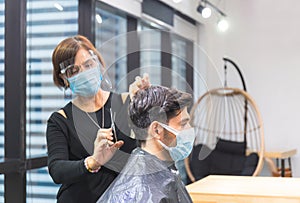 Young man getting haircut by hairdresser, Barber using scissors and comb, New normal concept