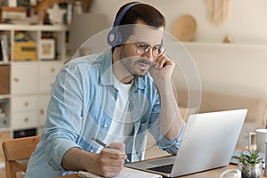 Young man getting remote education sitting by laptop in headphones