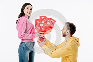 Young man gifting bouquet of red paper cut cards with hearts symbols to pretty girl isolated on white