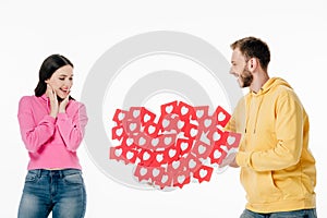 Young man gifting red paper cut cards with hearts symbols to smiling girl isolated on white