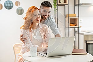 Young man and ginger woman have fun shopping online together on computer.