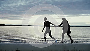 Young man and girl running along the embankment at sunset, slow motion