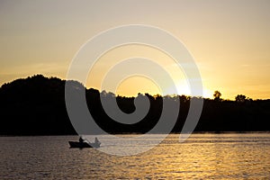 A young man and a girl are sitting in a boat and floating on the river at sunset. Silhouette of a couple