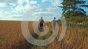 A young man and a girl with sports figures in sportswear are running along a cereal field.