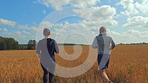 A young man and a girl with sports figures in sportswear are running along a cereal field.