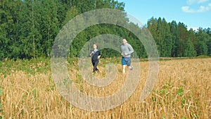 A young man and a girl with sports figures in sportswear are running along a cereal field.