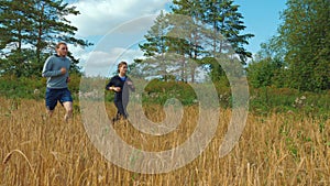 A young man and a girl with sports figures in sportswear are running along a cereal field.