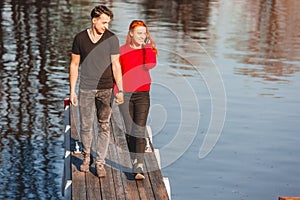 A young man and a girl walk side by side along a wooden pier