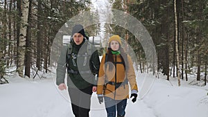 A young man and a girl are walking along a winter forest path.
