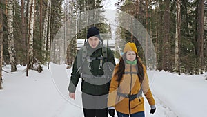 A young man and a girl are walking along a winter forest path.
