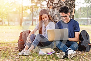 Young man and girls friend classmates sitting at park under tree