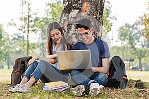 Young man and girls friend classmates sitting under tree consult