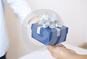 Young man give a gift in a box,holding blue Gift box with bow over holiday background which celebrating  couple image