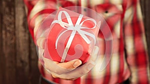 Young man gives a gift on wooden background. Red gift box with white ribbon opening. Congratulate Happy New Year, Merry