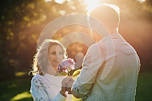Young man giving his smiling wife flowers at sunset