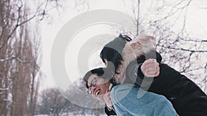 Young man giving piggyback ride to his girlfriend and spinning her in the park on snowy winter day. Newlywed asian