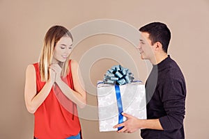 Young man giving present to his beloved girlfriend on color background