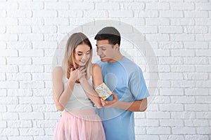 Young man giving present to his beloved girlfriend near white brick wall