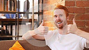 Young man giving thumbs up while smiling at work , office