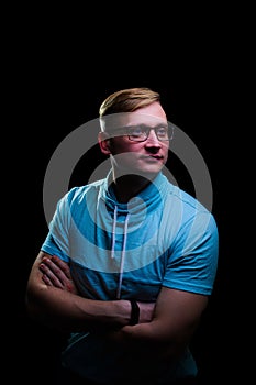 Young man in glasses and a blue t-shirt stands with a pensive look on a black background