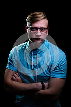 Young man in glasses and a blue t-shirt stands with a pensive look on a black background