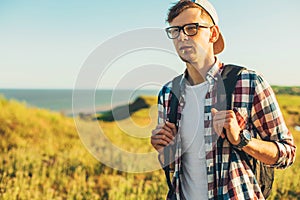 Young man, in glasses and in a cap with a backpack, hiking and enjoying the mountain landscape, adventure man hiking in the desert