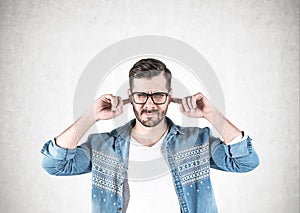 Young man in glasses covering ears