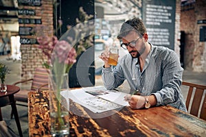 Young man with glasses and casual wear reading newspaper in cafe, sitting alone